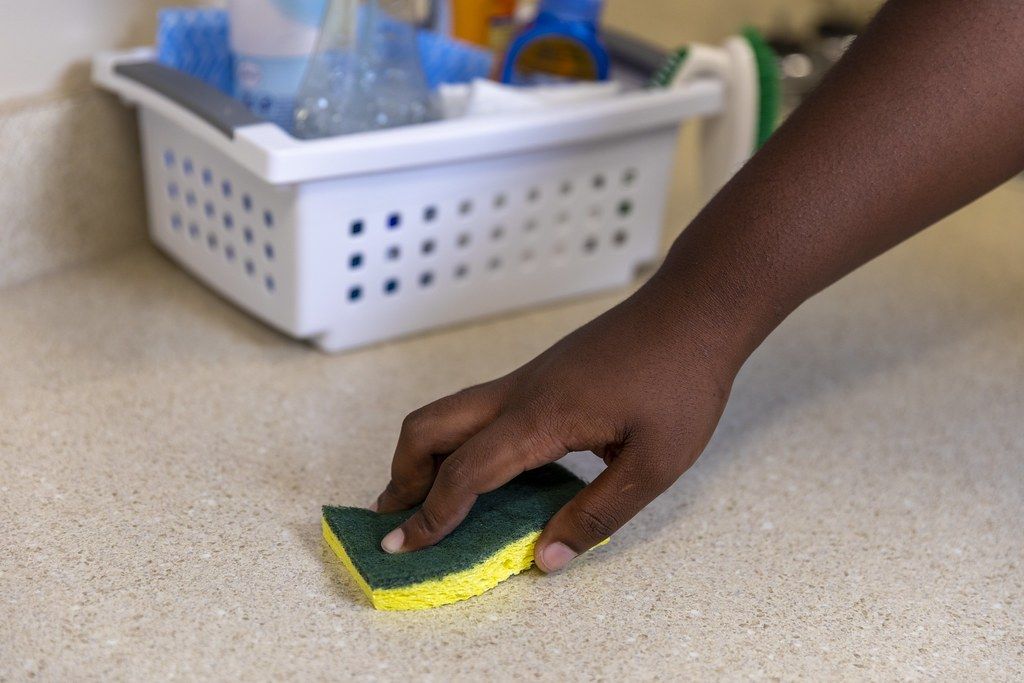 Mano limpiando el mesón de una cocina con esponja